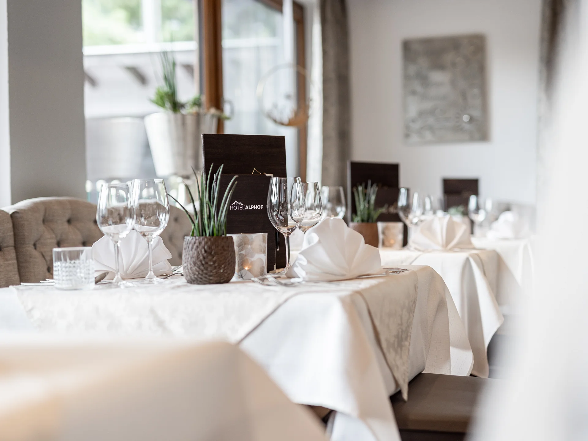 Der Alphof | Ihr Hotel in Fulpmes Elegant gedeckter Restauranttisch mit Weingläsern, weißen Servietten und Pflanze