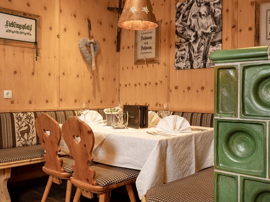 Mein Hotel in Fulpmes im Stubaital Gemütliche Holzstube mit Tisch, Sitzbank, zwei Holzstühlen und grünem Kachelofen