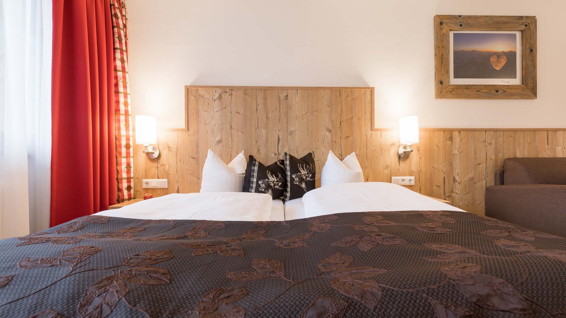 Stubaital: family hotel for holidays in comfort Cozy double bed with wooden headboard and brown bedspread in a bright room