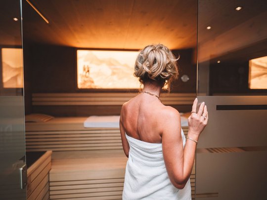 Mein Hotel in Fulpmes im Stubaital Frau mit Handtuch betritt eine Sauna mit warmer Beleuchtung