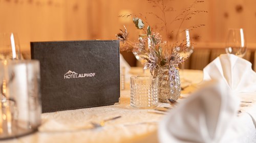 Mein Hotel in Fulpmes im Stubaital Eleganter gedeckter Tisch mit Hotel Alphof Speisekarte und Blumendekoration