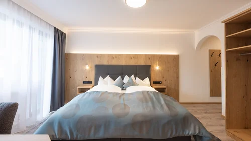 Der Alphof | Ihr Hotel in Fulpmes Helles Schlafzimmer mit Doppelbett, Holzvertäfelung und offenem Kleiderschrank