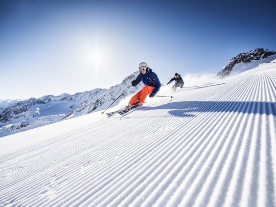 Mein Hotel in Fulpmes im Stubaital Zwei Skifahrer fahren auf frisch präparierter Piste bei sonnigem Wetter
