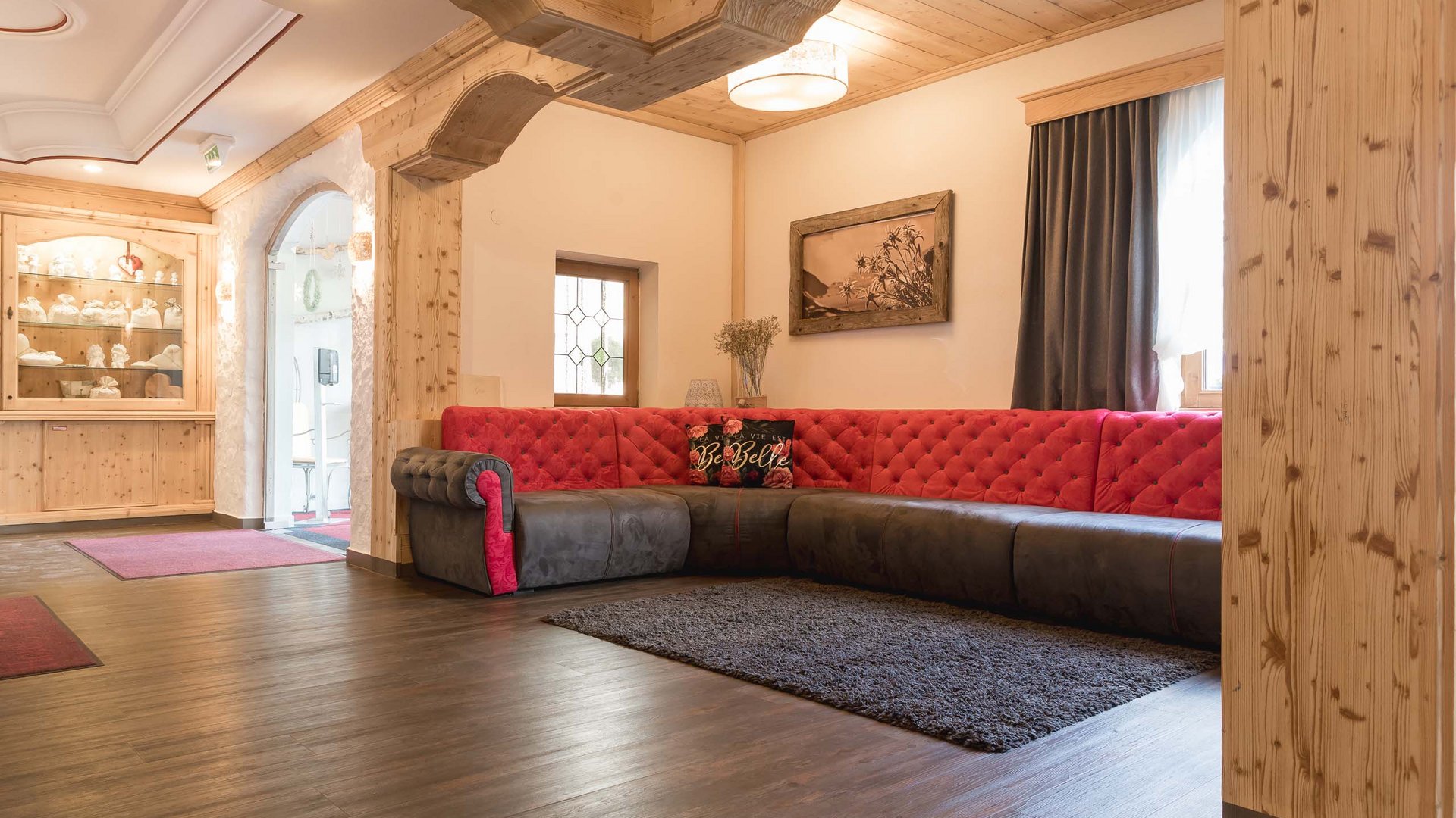 Mein Hotel in Fulpmes im Stubaital Gemütliches Wohnzimmer mit rotem und grauem Ecksofa und Holzbalkendecke