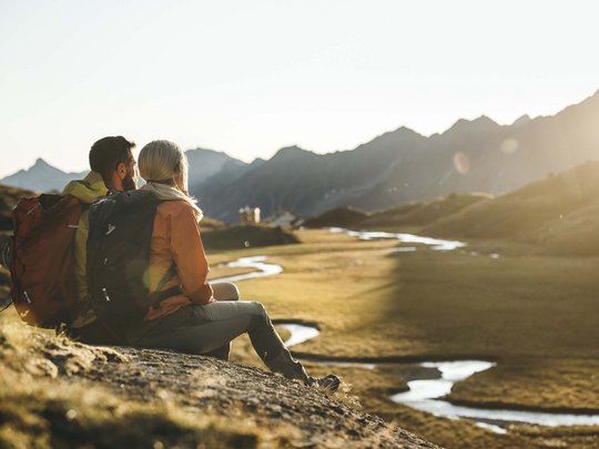 Mein Hotel in Fulpmes im Stubaital Paar mit Rucksäcken sitzt auf Felsen und schaut auf Berglandschaft im Sonnenuntergang