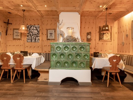 Romance in the mountains Cozy dining room with green tiled stove, wooden chairs, and corner bench seating