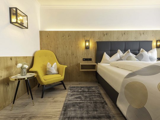 Mein Hotel in Fulpmes im Stubaital Modernes Schlafzimmer mit gelbem Sessel, kleinen Tisch und grauem Teppich