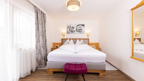 Mein Hotel in Fulpmes im Stubaital Hell eingerichtetes Schlafzimmer mit Doppelbett, Nachttischen und lila Hocker