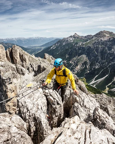 Der Alphof | Ihr Hotel in Fulpmes Bergsteiger in gelber Jacke auf einem felsigen Grat vor alpiner Berglandschaft